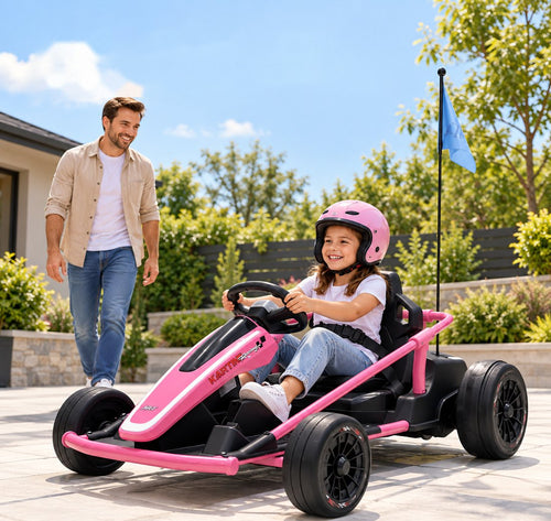 A smiling girl in a pink helmet drives the rose go-kart across a paved patio as her dad walks beside her